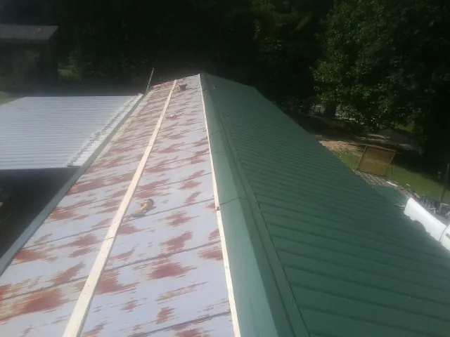 Old rusted panels beside newly installed green metal roofing — Wind Damage Roof Repair by Roofing Brothers in Williams